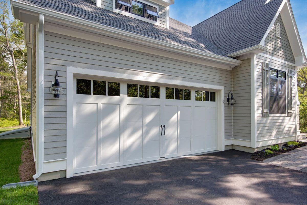 White carriage house garage door with transom windows on a sunny day with dappled light