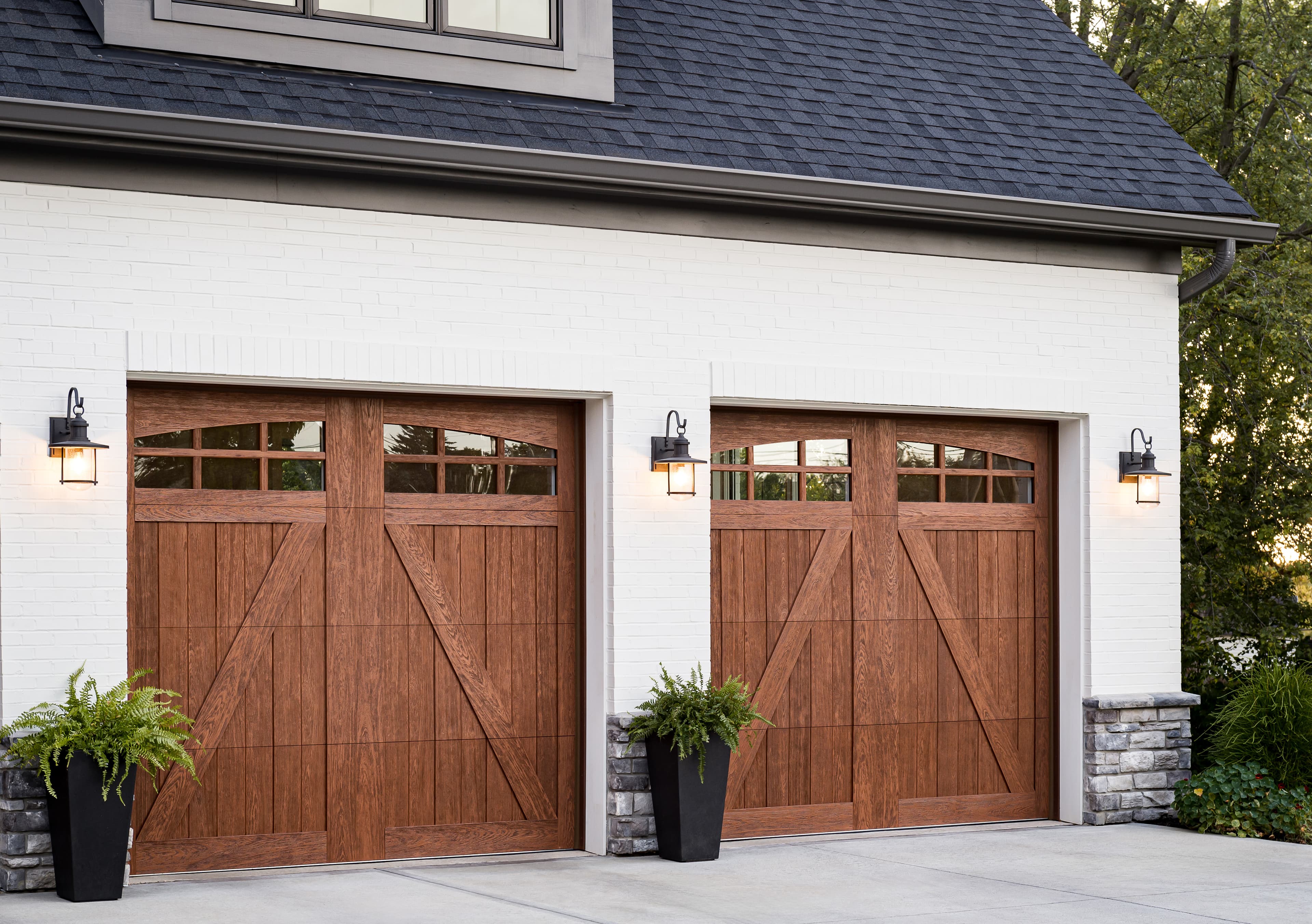 Insulated carriage house garage doors with warm wood finish on white brick home at dusk