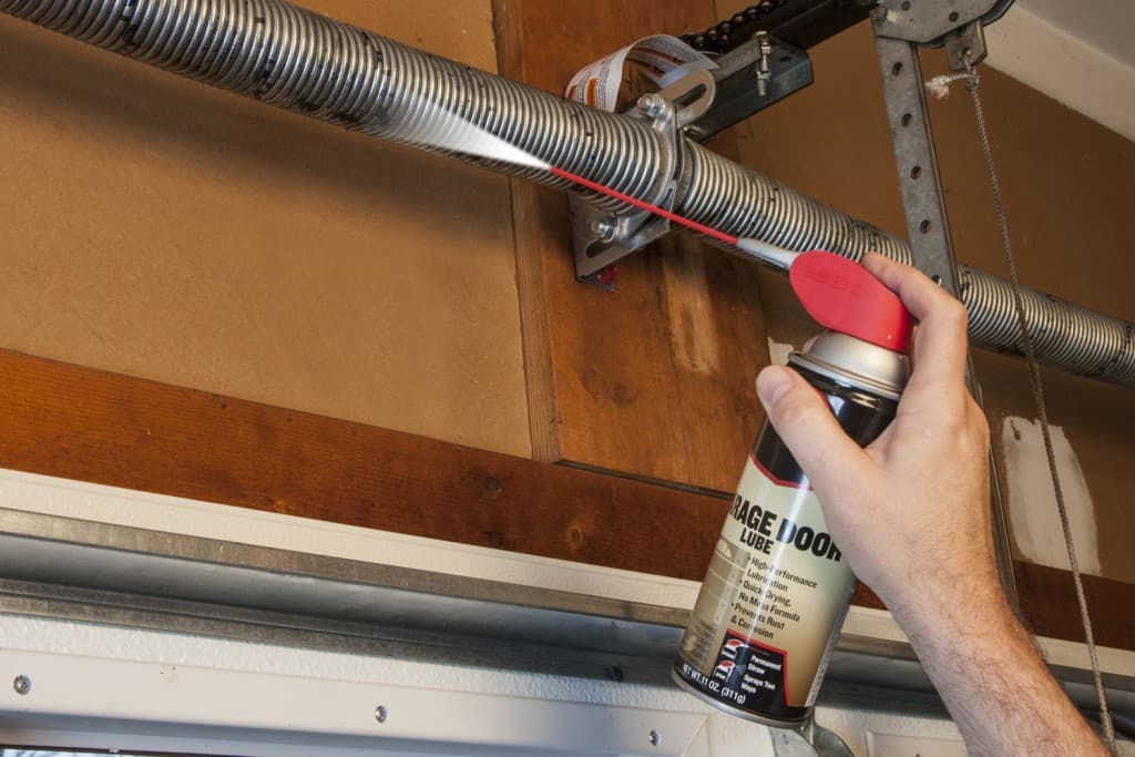 Technician lubricating garage door torsion spring with professional spray lubricant