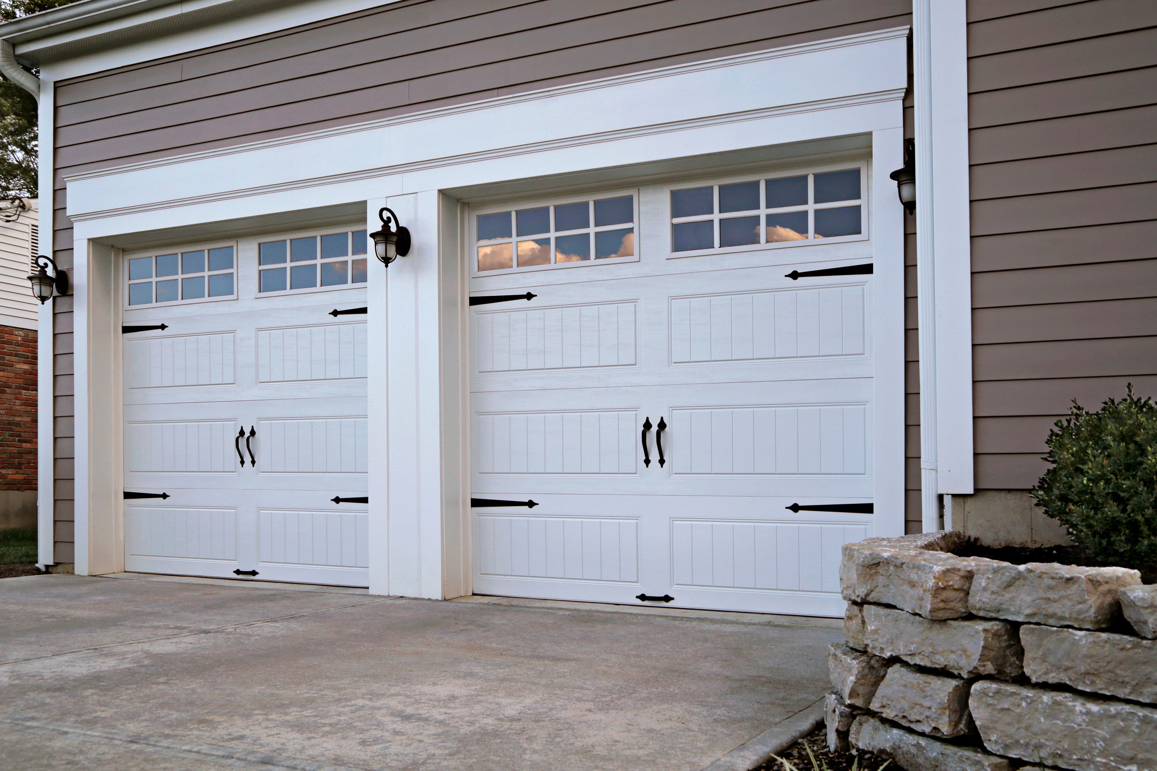 Clean white carriage house garage doors on stone facade with pristine curb appeal