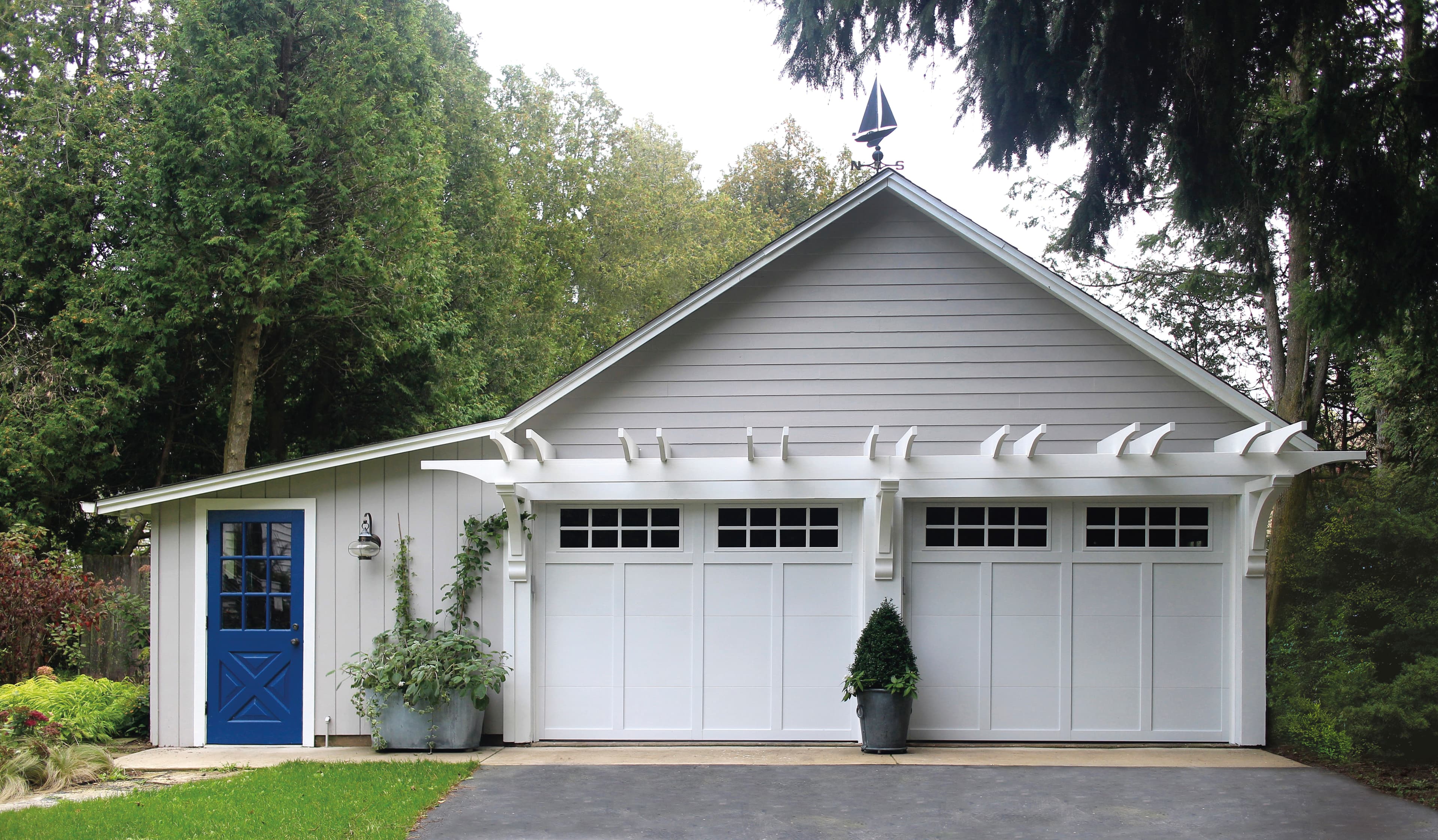 Charming cottage-style garage with white carriage doors surrounded by lush greenery