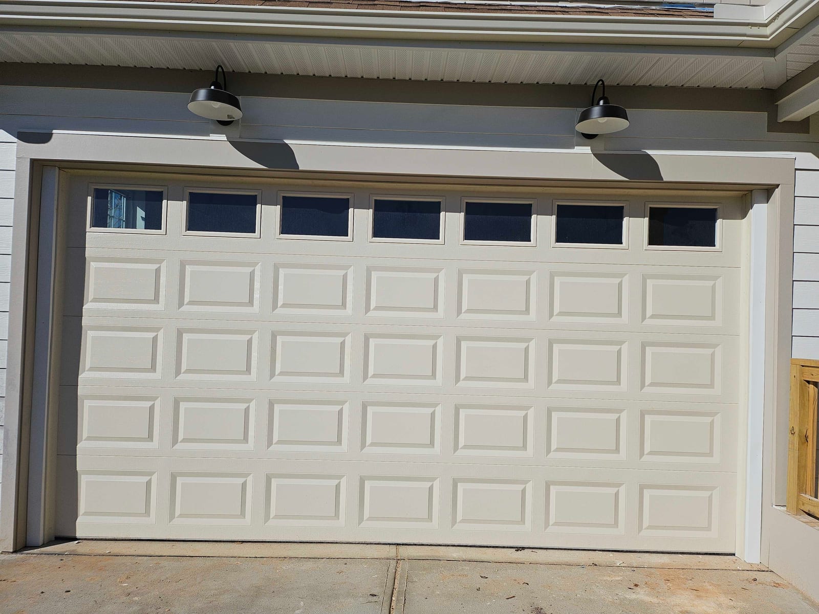 New construction two-car raised-panel door with gooseneck lanterns and gray beam accent