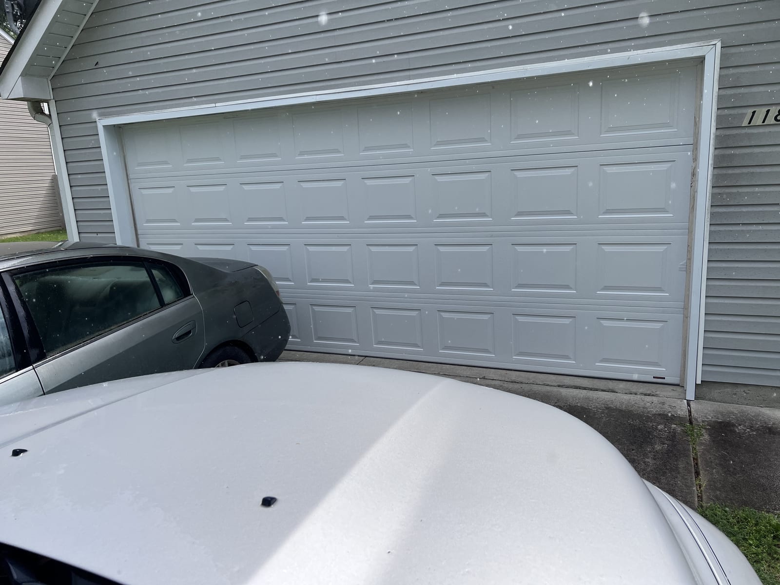 New white raised-panel garage door completed on gray siding home exterior